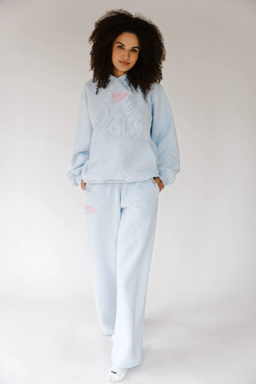 A woman modeling a light blue textured knit lounge set consisting of a long-sleeve top and matching wide-leg pants, with small pink embroidered details on the chest and thigh.