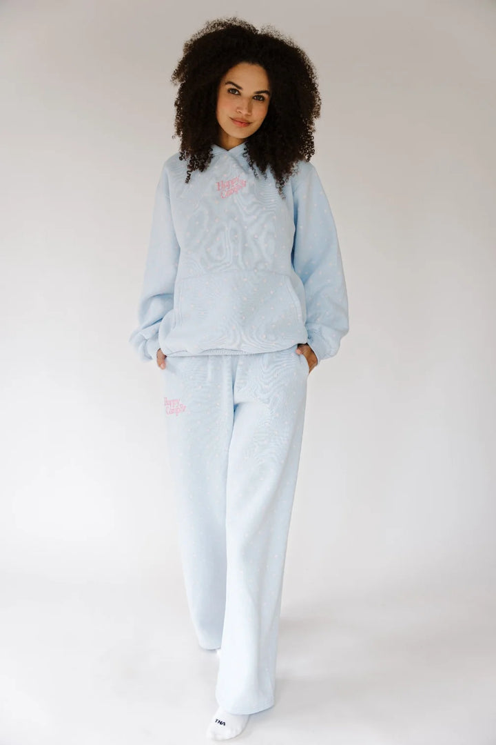 A woman modeling a light blue textured knit lounge set consisting of a long-sleeve top and matching wide-leg pants, with small pink embroidered details on the chest and thigh.