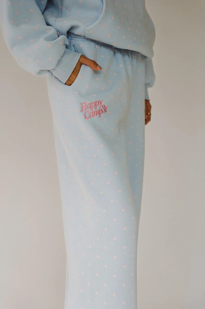 A person wearing a light blue sweatshirt and matching sweatpants with small pink polka dots. The sweatpants have a side pocket with 'Happy Camp4r' embroidered in pink script, and the person is shown from the chest down against a plain light background.