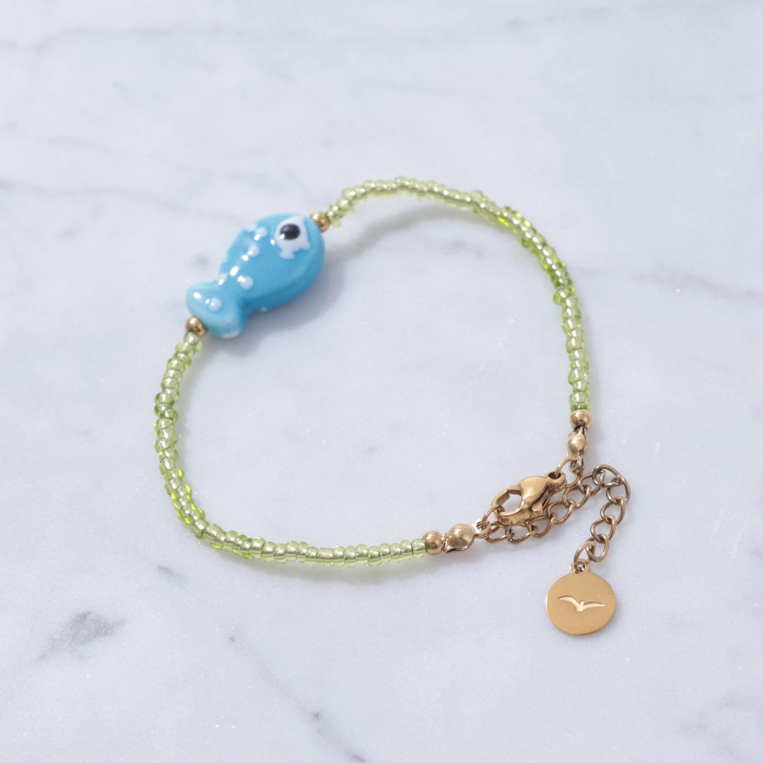 Bracelet with blue fish charm and gold accents on a marble background