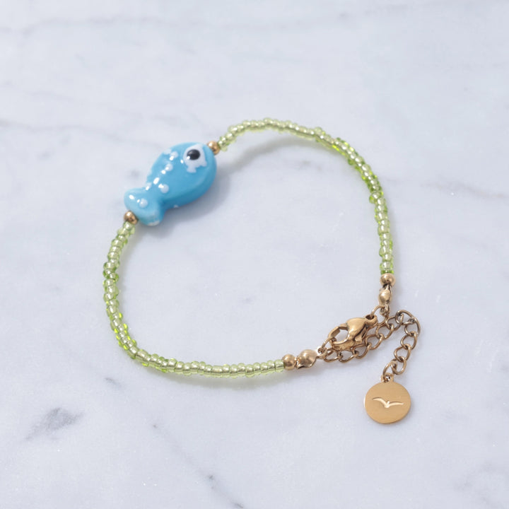 Bracelet with blue fish charm and gold accents on a marble background