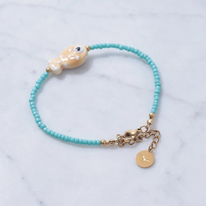 Turquoise beaded bracelet with a gold charm on a marble background
