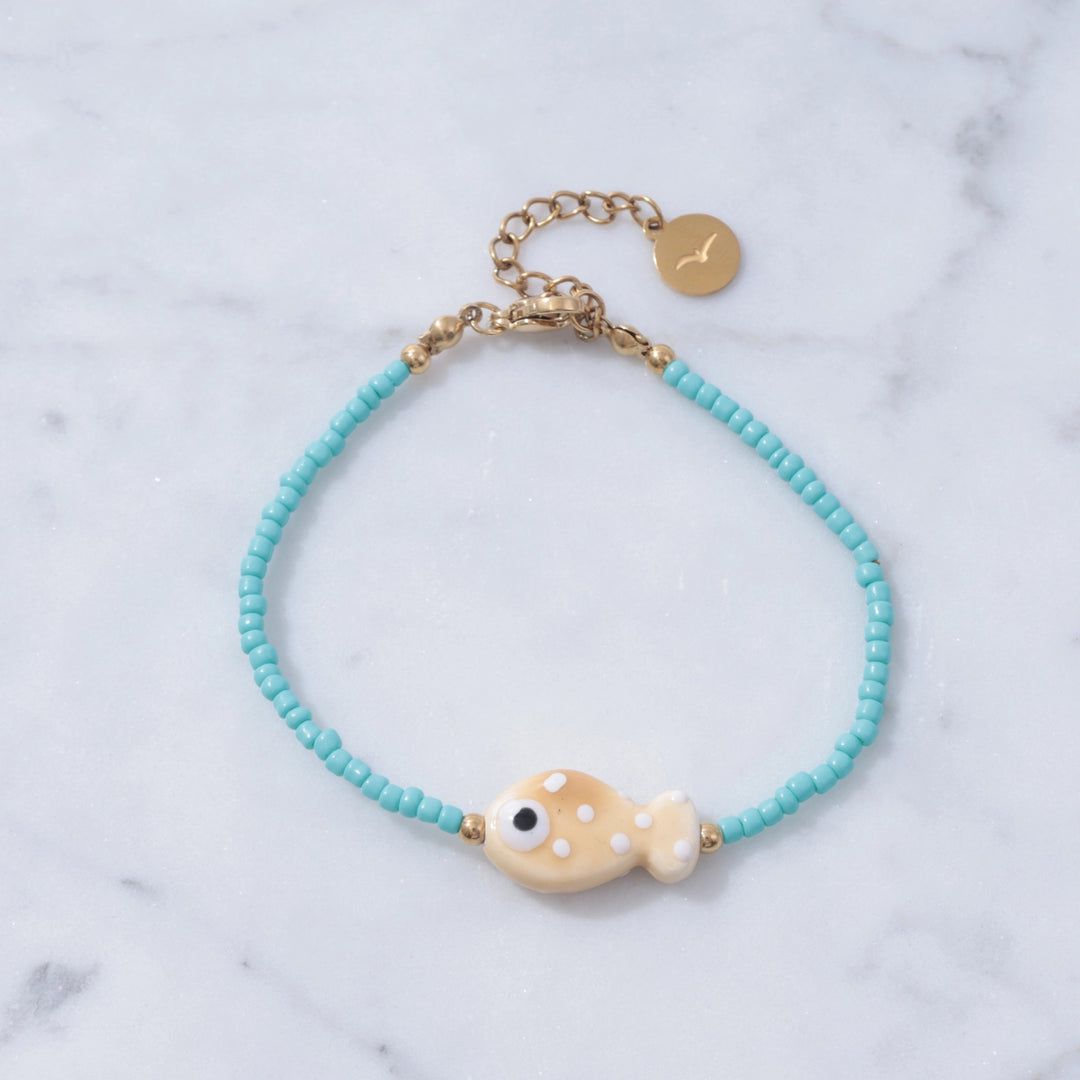 Bracelet with turquoise beads and a gold fish charm on a marble background