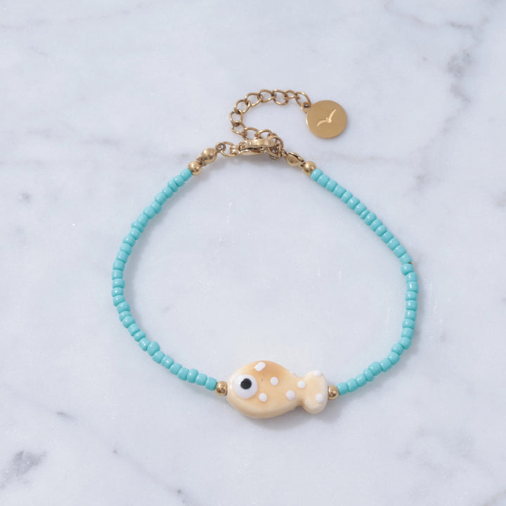 Bracelet with turquoise beads and a gold fish charm on a marble background