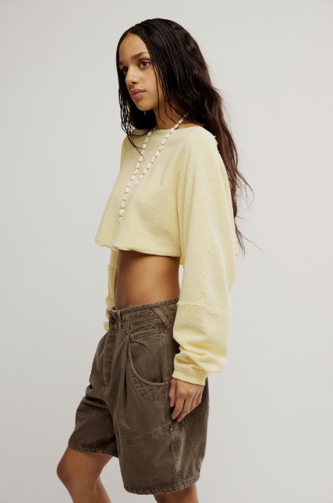 Woman wearing a light yellow long-sleeve top and brown shorts on a plain background