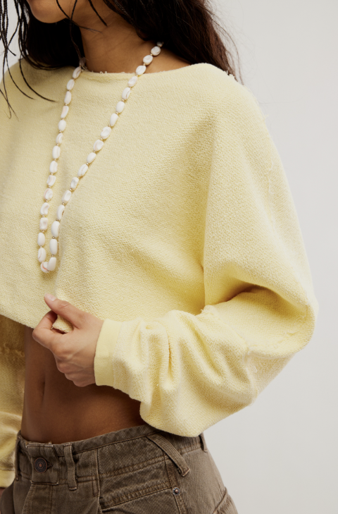 Person wearing a yellow sweater and pearl necklace on a plain background