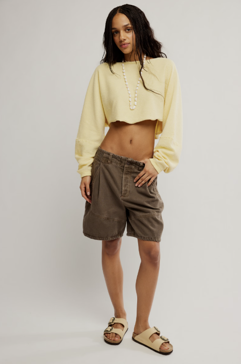 Woman wearing a yellow cropped sweater and brown shorts on a plain background