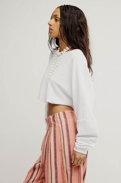 Woman wearing a white cropped sweater with pearl details and pink striped pants against a plain background