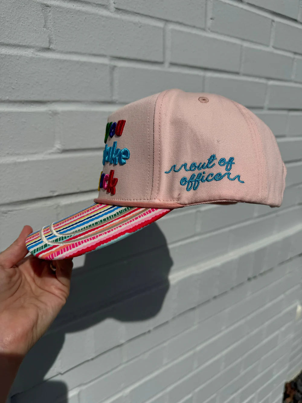 Pink cap with colorful text against a gray brick wall