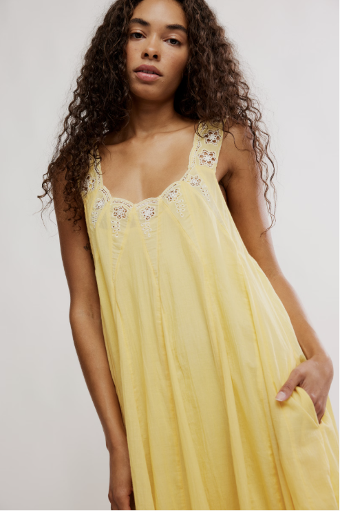 Woman wearing a yellow dress with floral embellishments against a plain background