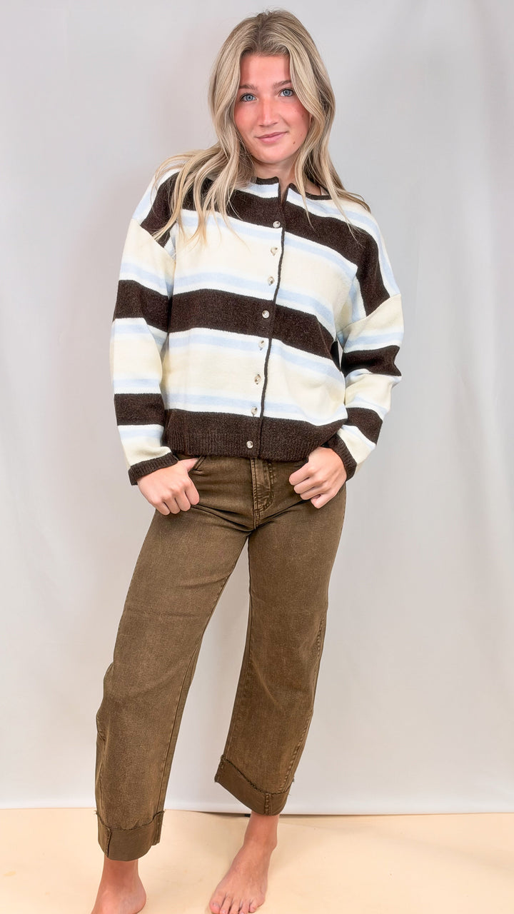 Woman wearing striped cardigan with brown jeans on plain background