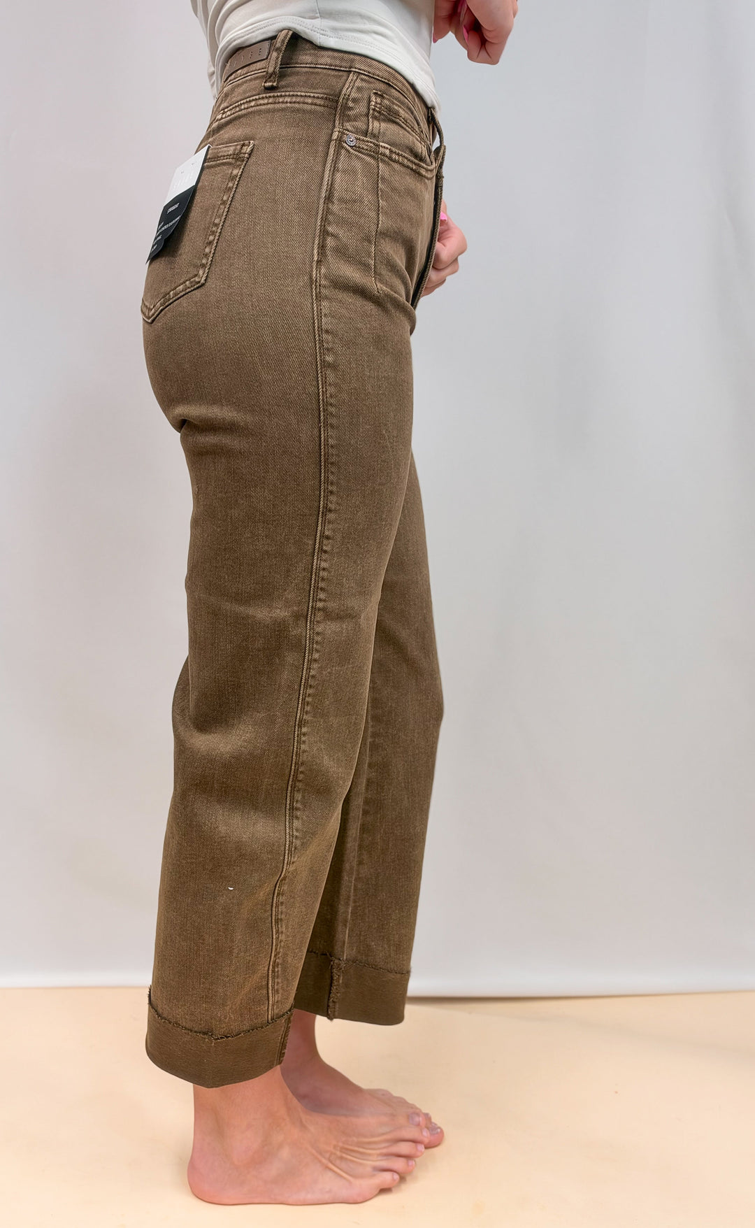 Woman shown from side view wearing brown jeans on plain background