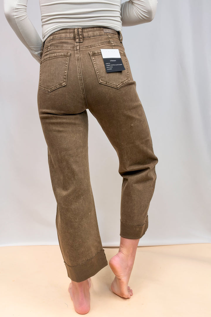 Woman shown from back view wearing brown jeans on plain background