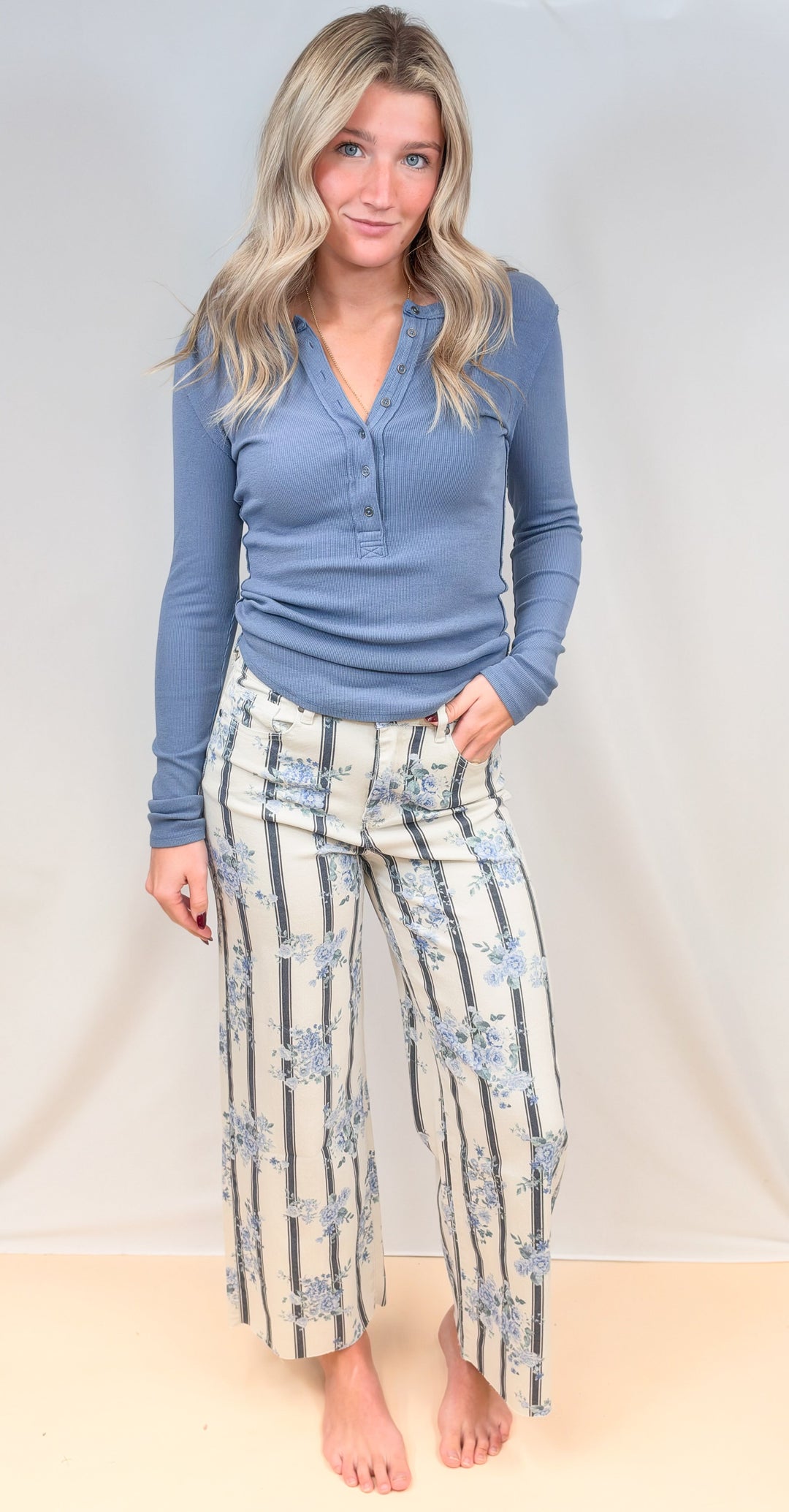 Woman wearing blue long sleeve top and white and blue stripe pants with floral print on plain background