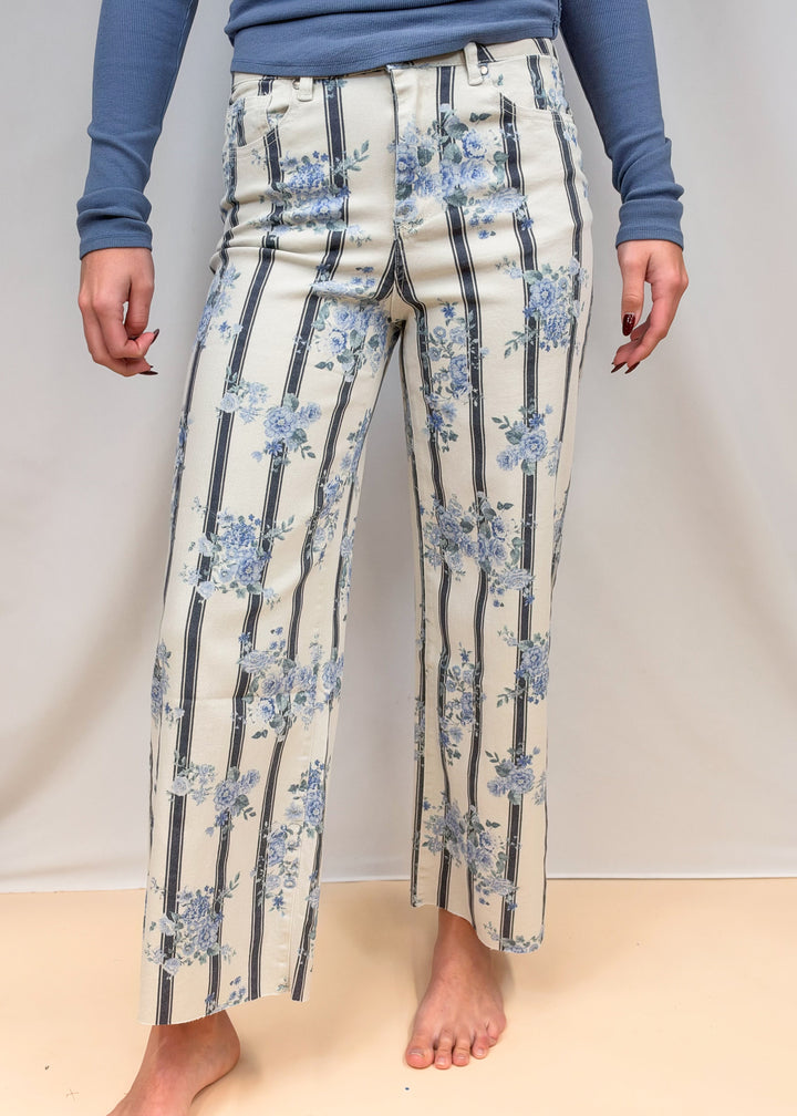 Woman shown from waist down wearing blue and white stripe pants with floral detail on plain background
