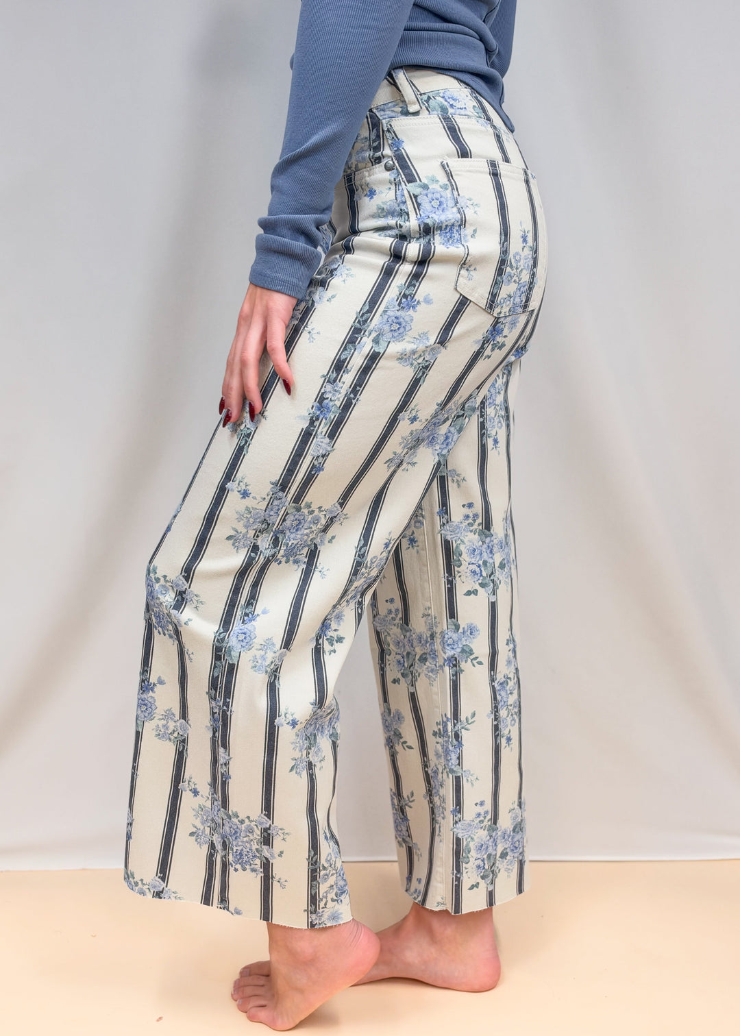 Woman shown from side view waist down wearing white and blue pants with floral detail on plain background