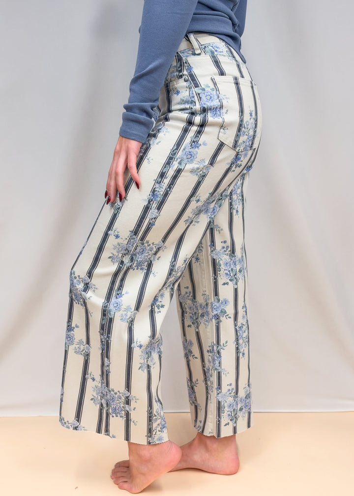 Woman shown from side view waist down wearing white and blue pants with floral detail on plain background