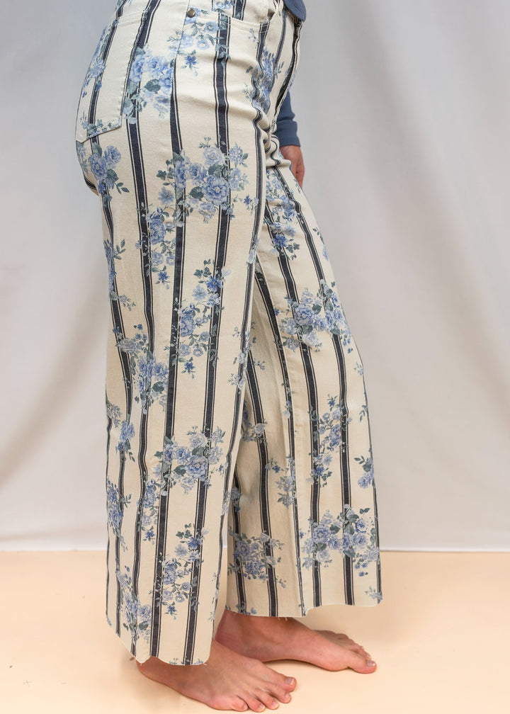 Woman shown from side view waist down wearing white and blue stripe pants with floral detail on plain background