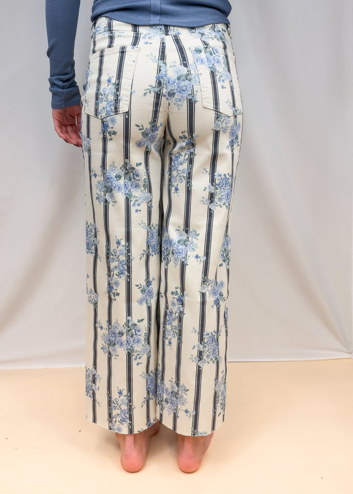 Woman shown from back view waist down wearing white and blue stripe pants with floral detail on plain background