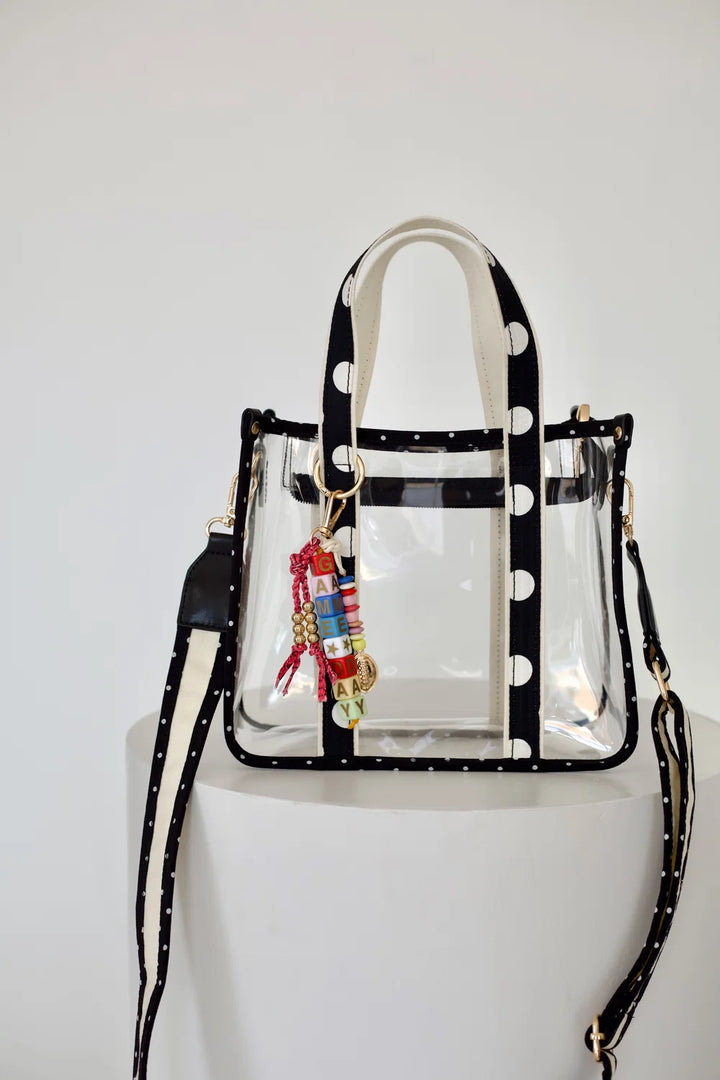 Clear tote bag with polka dot handles and bag charm on plain background