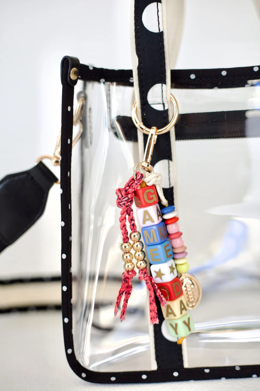 Close up of clear tote with polka dot handle and gameday bag charm on plain background