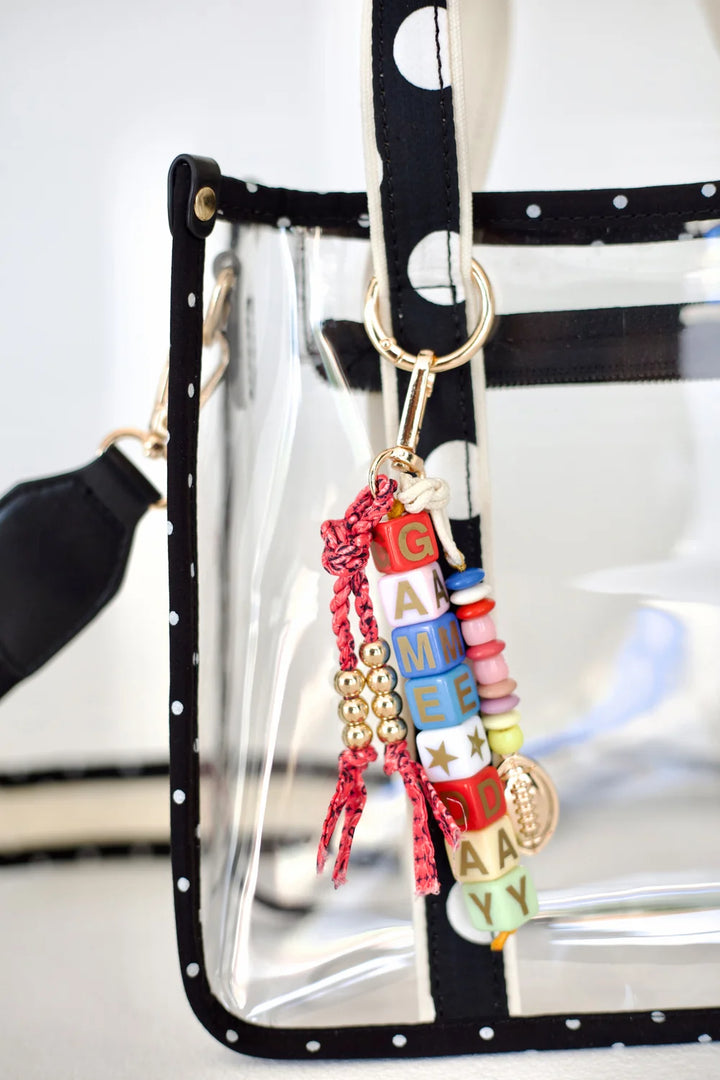 Close up of clear tote with polka dot handle and gameday bag charm on plain background