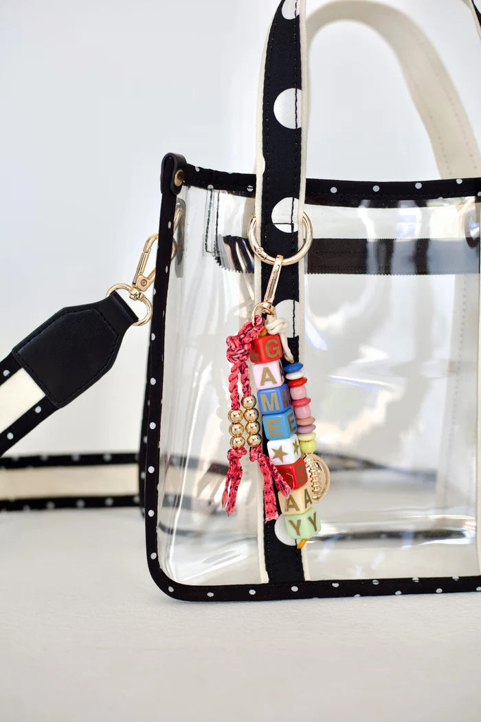 Close up of clear tote bag with polka dot handles and gameday bag charm on plain background