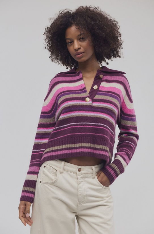 A woman modeling a cropped, long-sleeve knit polo cardigan with horizontal stripes in shades of purple, pink, and beige, paired with cream-colored jeans against a light gray studio background.