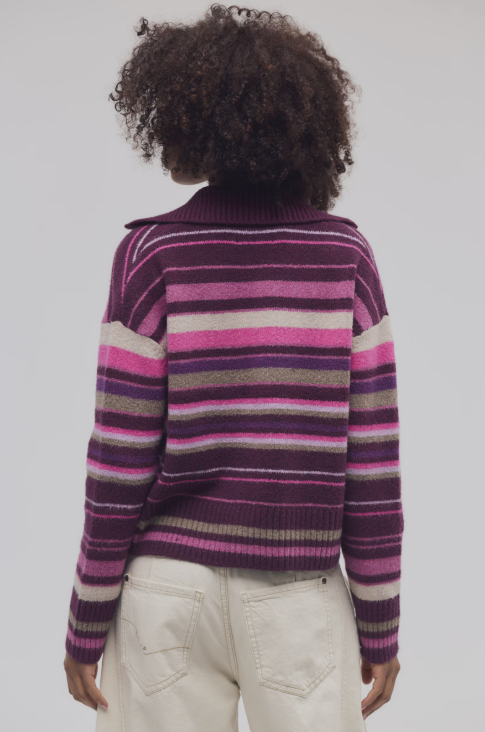 A person shown from the back wearing a fuzzy knit striped sweater with horizontal bands of purple, pink, beige, and gray, paired with off-white pants, against a light gray studio background.