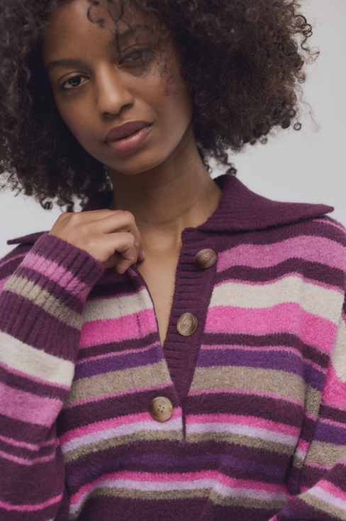 A close-up of a woman wearing a fuzzy knit cardigan with horizontal stripes in purple, pink, and beige, featuring a brown button placket.