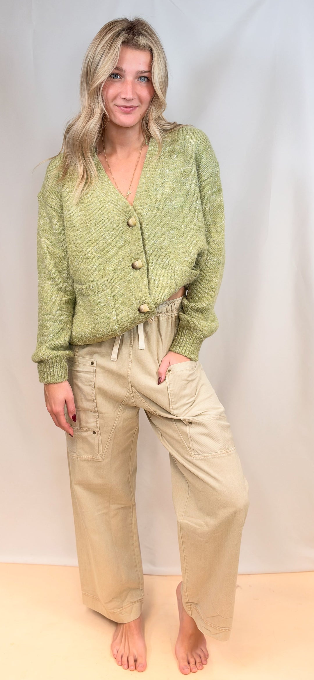 Woman wearing green cardigan sweater with beige pants on plain background