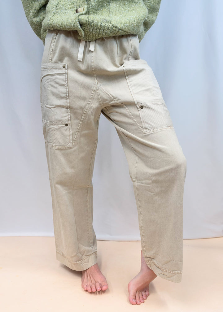 Woman shown from waist down wearing beige pants with rivet details on plain background