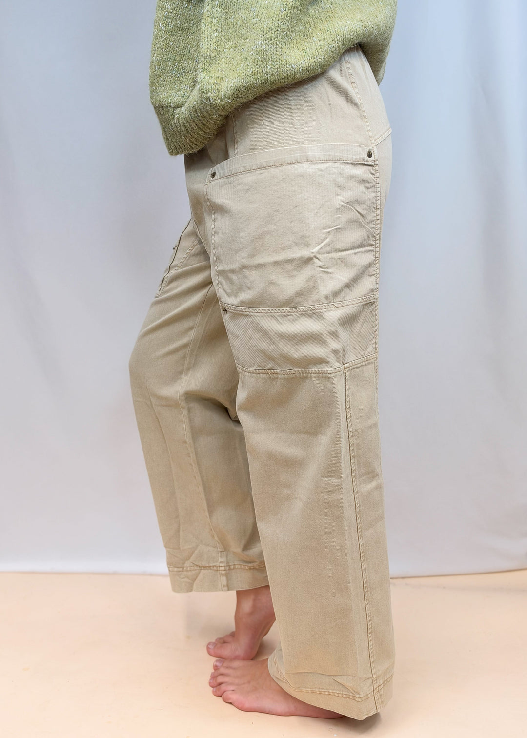 Woman shown from side view waist down wearing beige pants on plain background