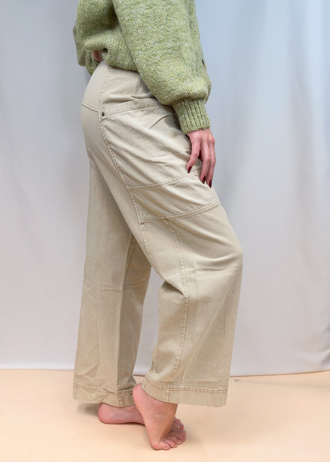Woman shown from side view wearing green sweater and beige pants on plain background