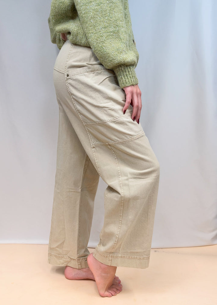 Woman shown from side view wearing green sweater and beige pants on plain background