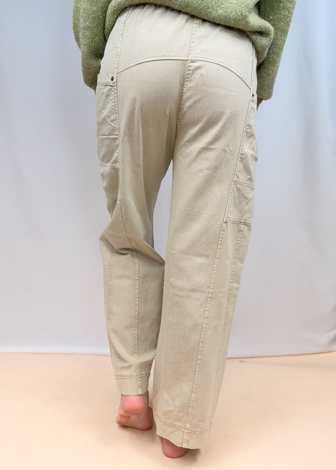 Woman shown from back view wearing green sweater and beige pants on plain background