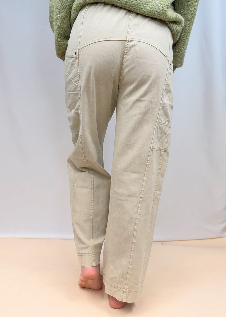 Woman shown from back view wearing green sweater and beige pants on plain background