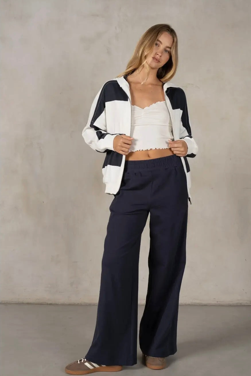 Woman wearing a navy and white striped cardigan over a white top and navy pants against a plain background
