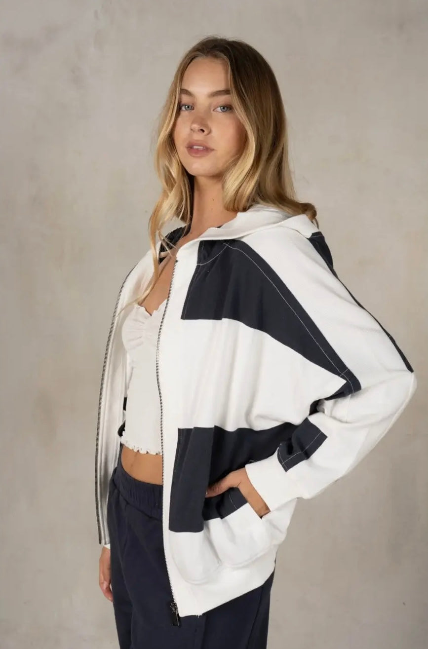 Woman wearing a white and  navy jacket against a neutral background