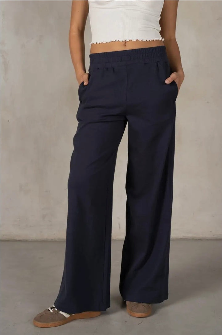 Person wearing navy wide-leg pants and a white top against a plain background