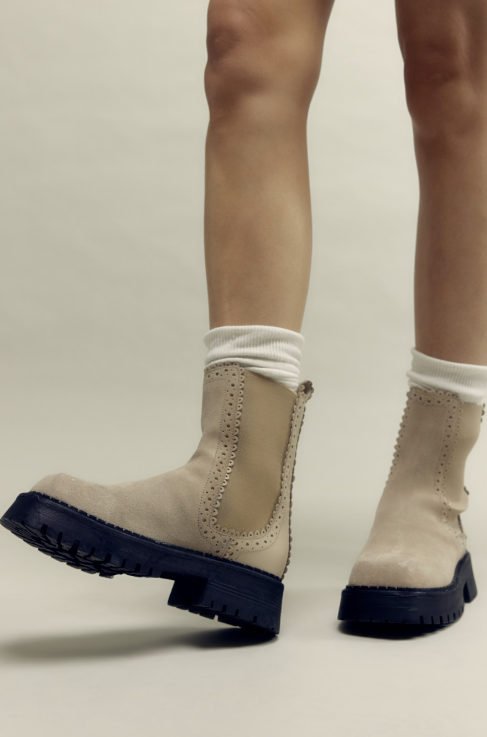 Woman wearing tan suede boots with chunky sole on plain background