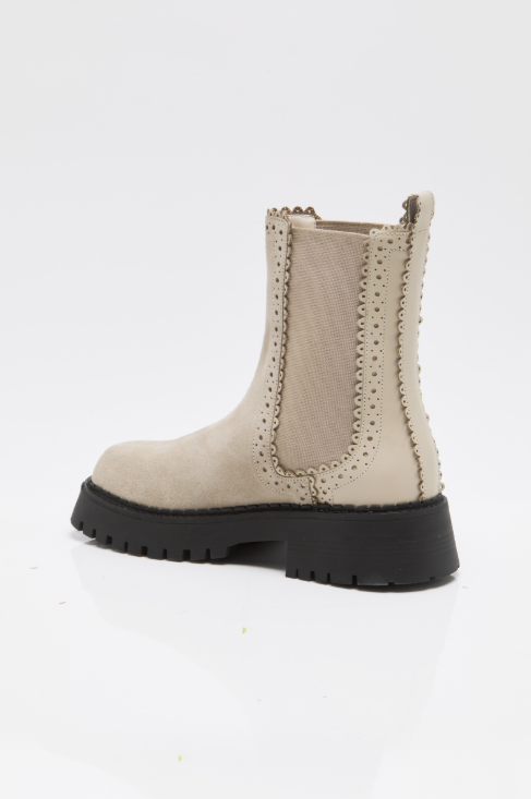 A single beige suede Chelsea-style ankle boot with decorative perforated stitching and a thick black lug sole, shown from a side profile on a white studio background.
