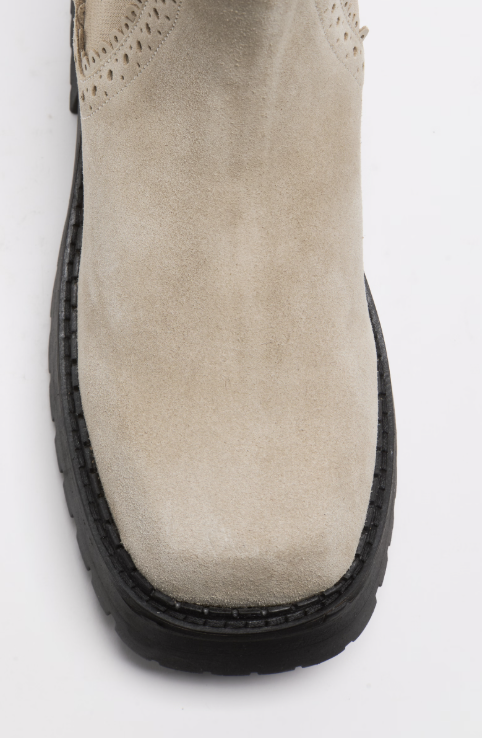 Close-up of the toe and sole of a beige suede ankle boot with a chunky black sole, shown on a white background.