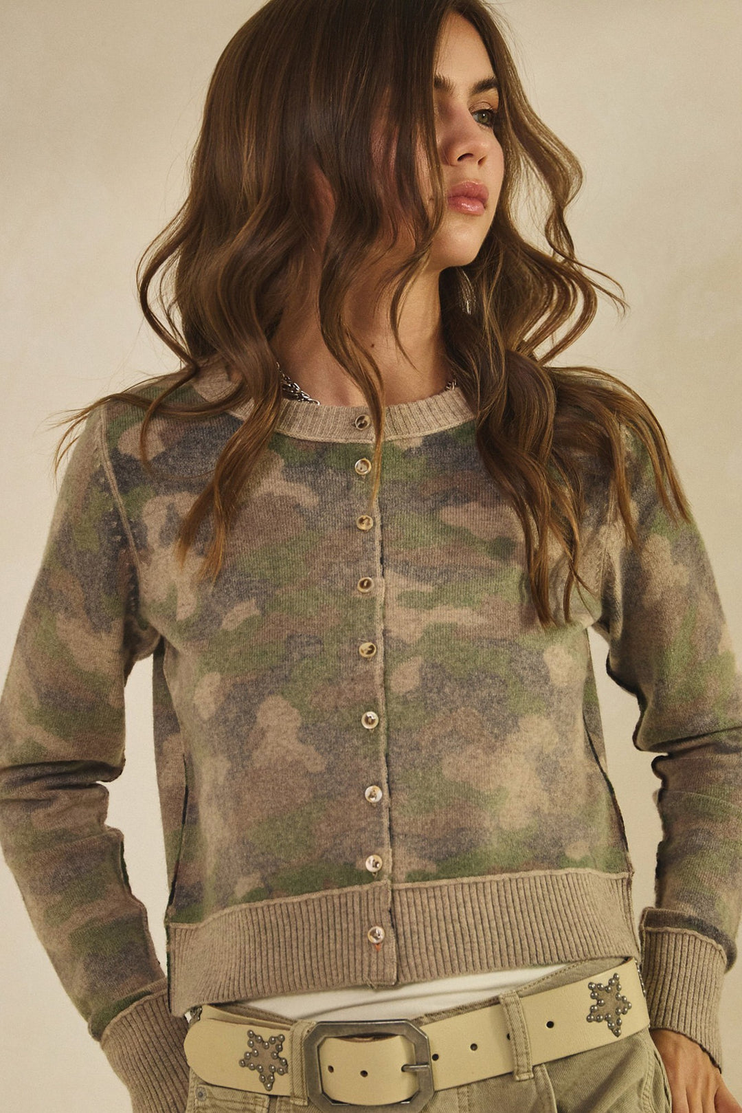 Woman wearing a camouflage cardigan against a neutral background
