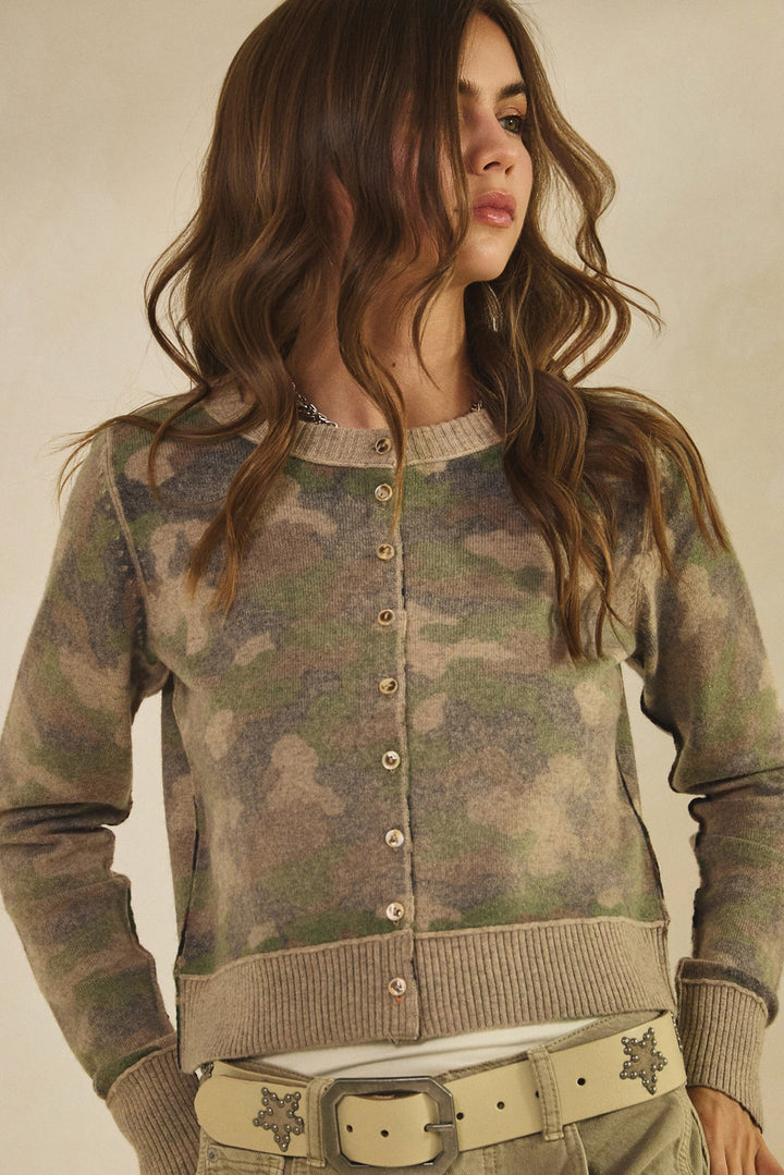 Woman wearing a camouflage cardigan against a neutral background