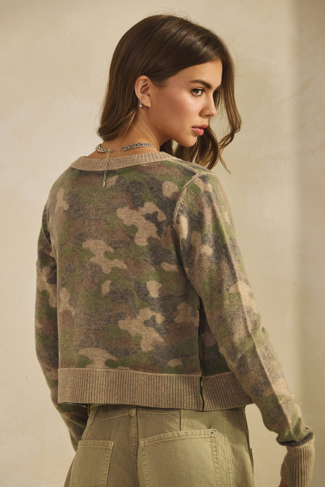 Woman wearing a camouflage sweater and beige pants against a neutral background