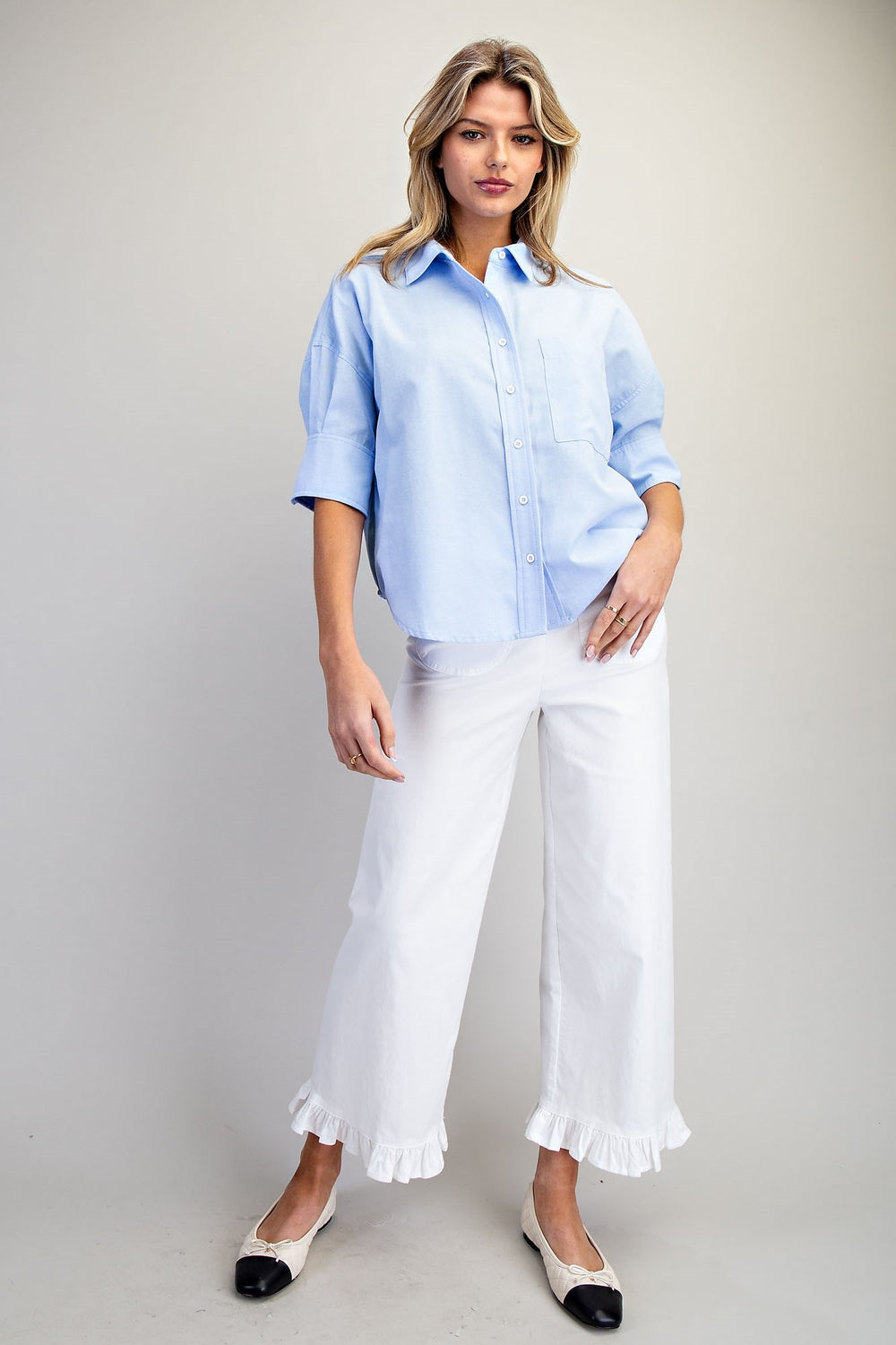 Woman wearing a light blue shirt and white pants on a plain background