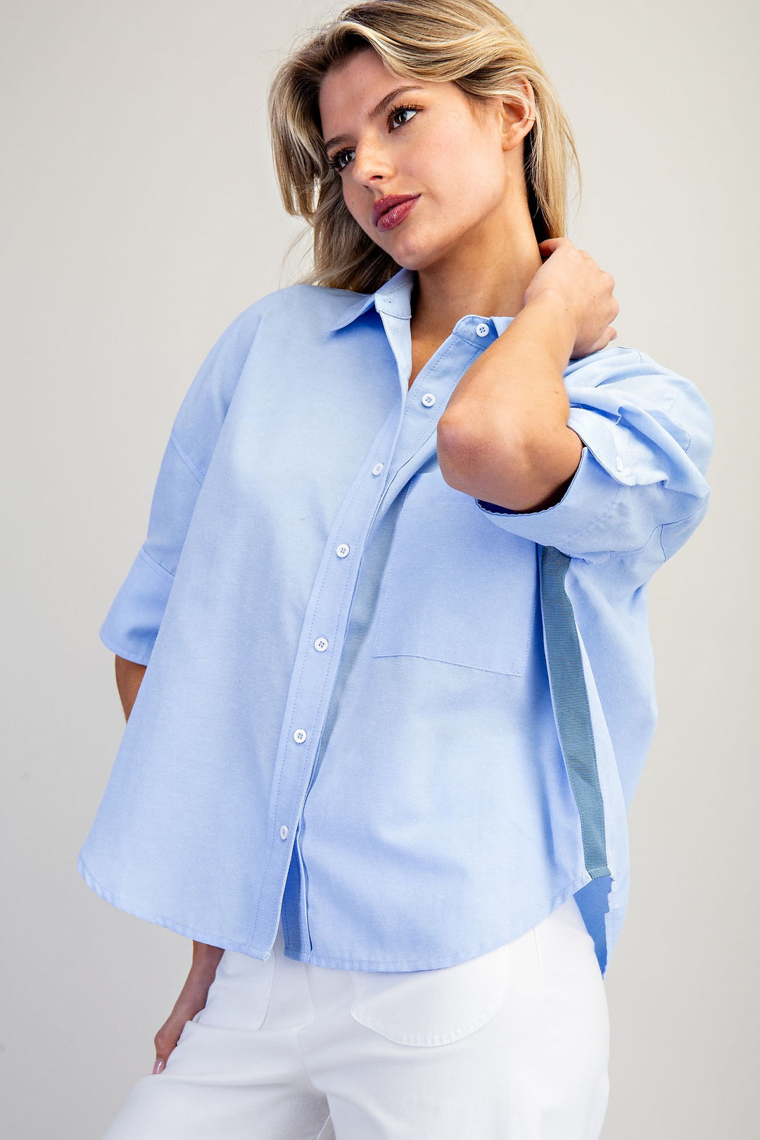 Woman wearing a light blue button-up shirt and white pants against a plain background