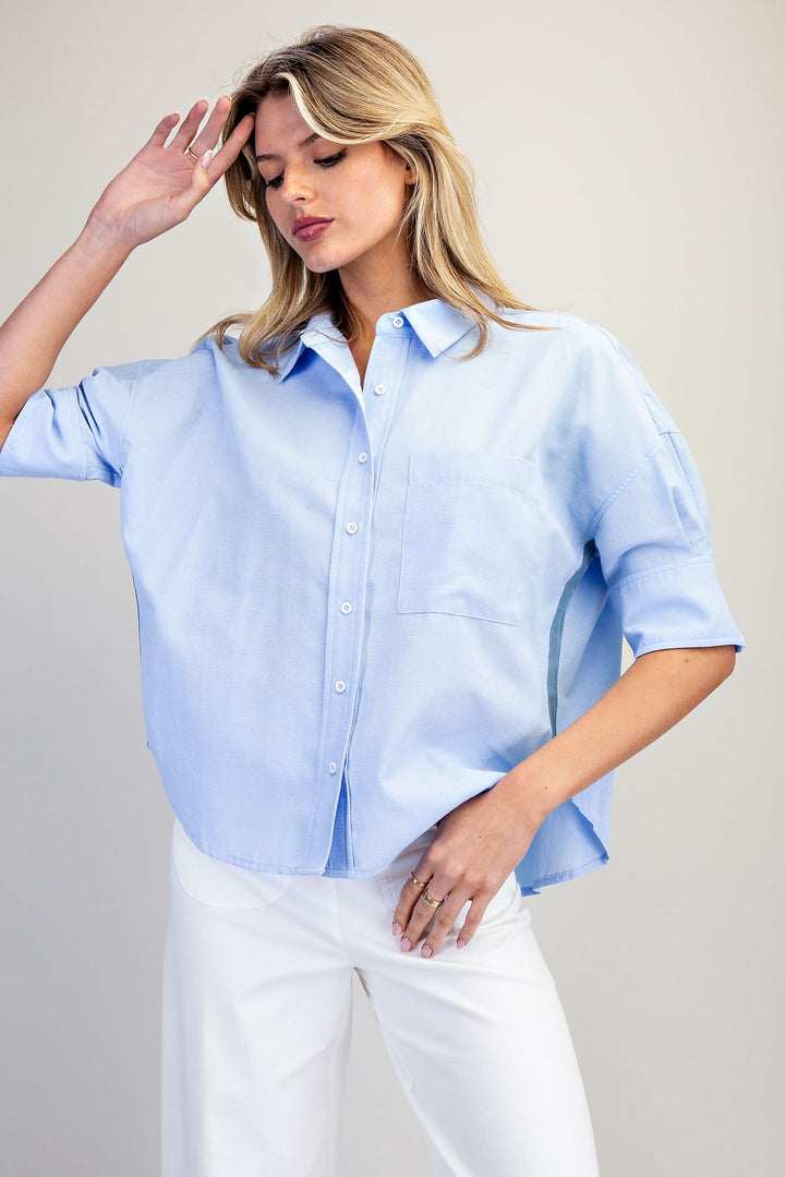 Woman wearing a light blue button-up shirt and white pants against a plain background