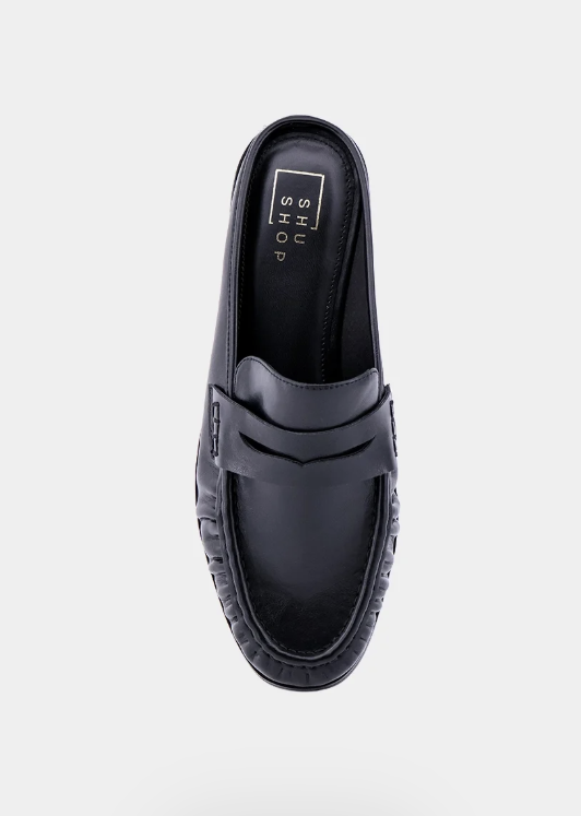 A single black leather penny loafer slip-on shoe shown from a top-down view on a light gray background. The brand name &